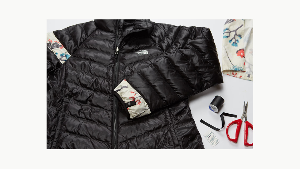 Black North Face jacket repaired with contrasting printed fabric beside sewing tools
